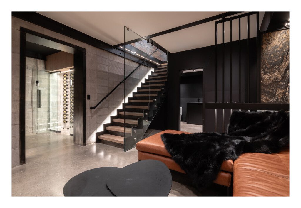 Modern industrial living room with a leather couch, glass wine cellar, and sleek staircase